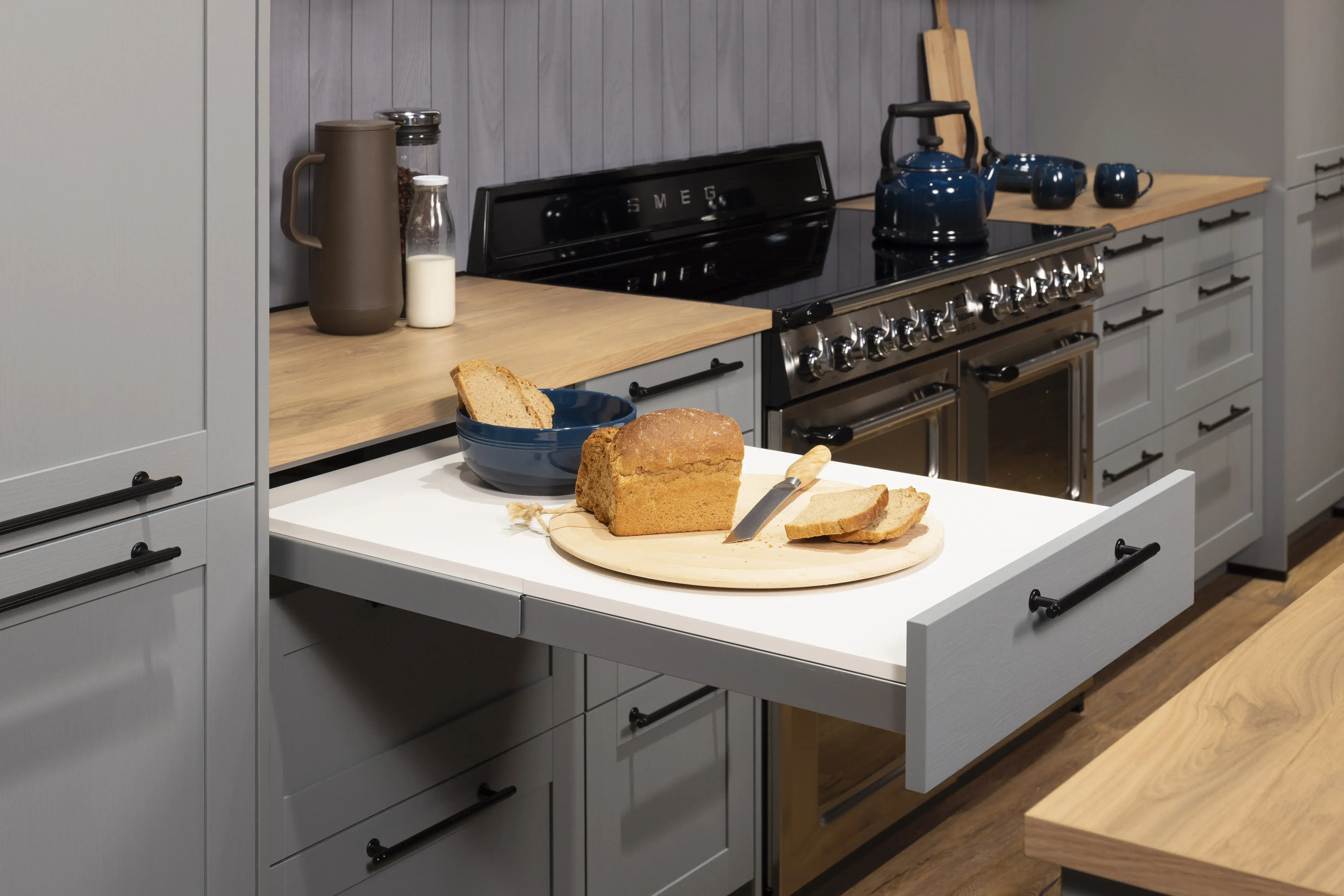 Graues Kücheninterieur mit ausgezogenem Brett, darauf Brot und Messer.