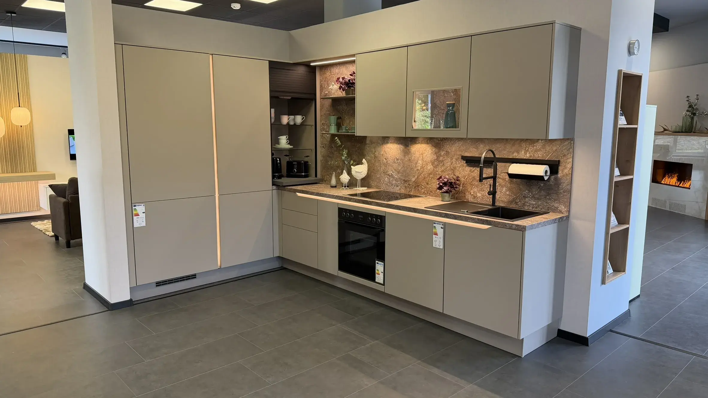 Moderne grifflose Küche in Greige mit Arbeitsplatte und Rückwand in Natursteinoptik sowie integrierter Beleuchtung