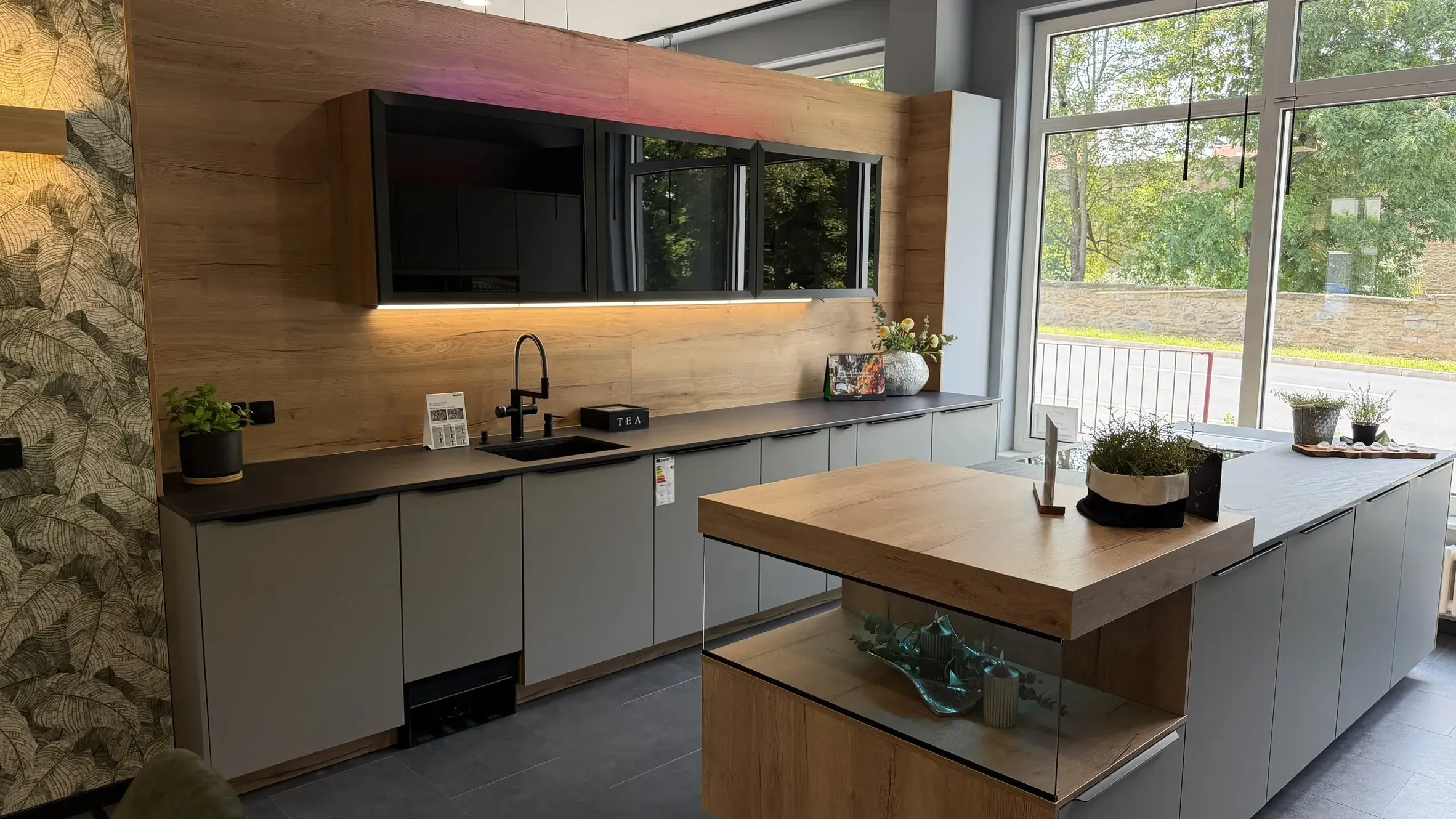 Moderne Designküche mit grauen Fronten, Kücheninsel, schwarzen Arbeitsflächen und warmen Holzelementen