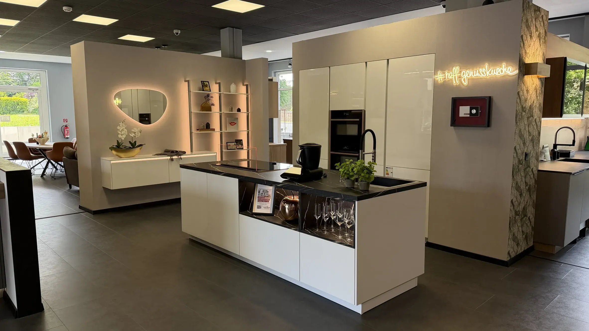 Elegante weiße Designküche mit Kochinsel, schwarzer Arbeitsplatte, integrierten Elektrogeräten und beleuchteten Regalen