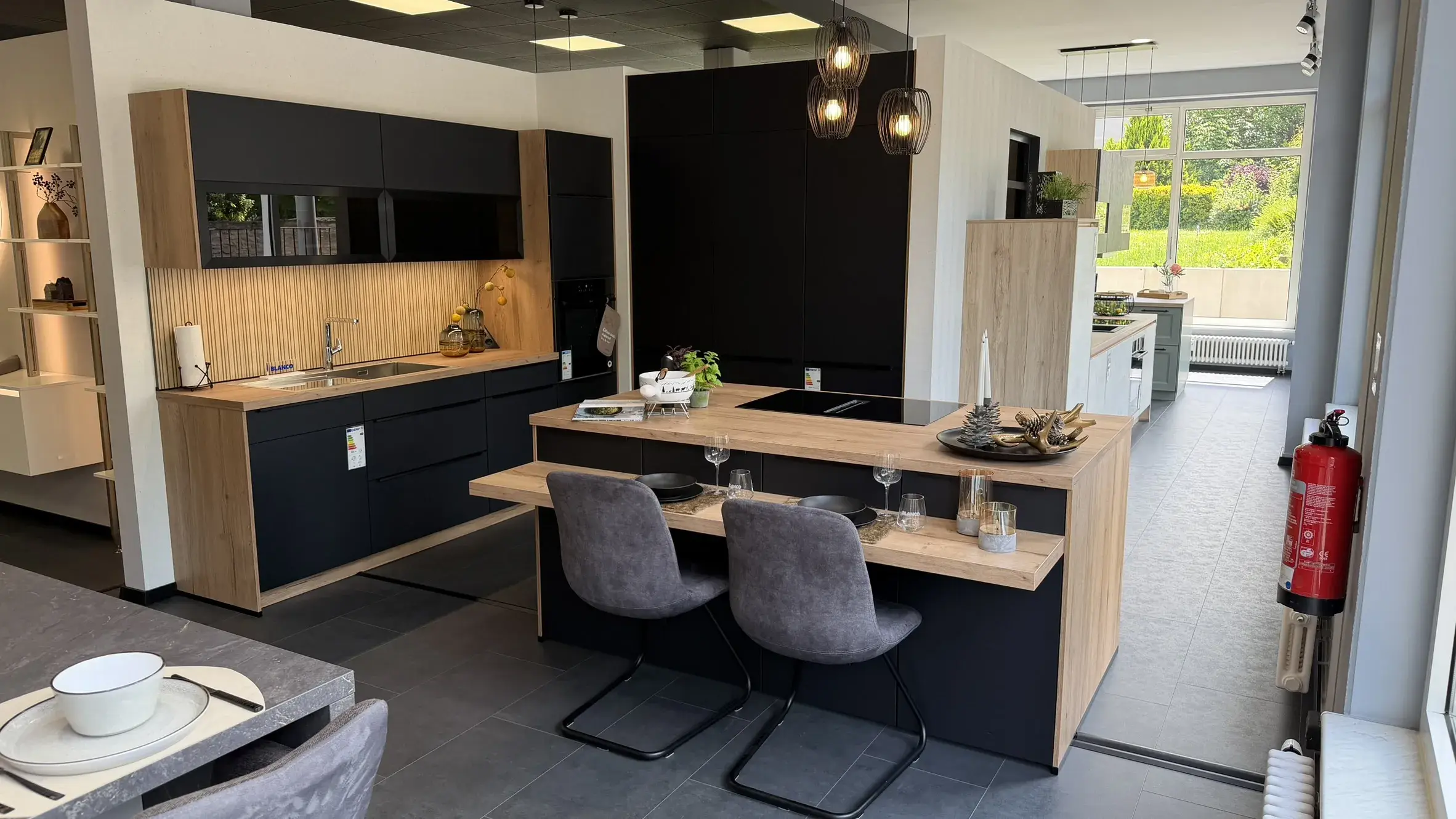 Moderne schwarze Küche mit Holzfronten, Kochinsel, integriertem Essplatz und stilvoller Pendelbeleuchtung