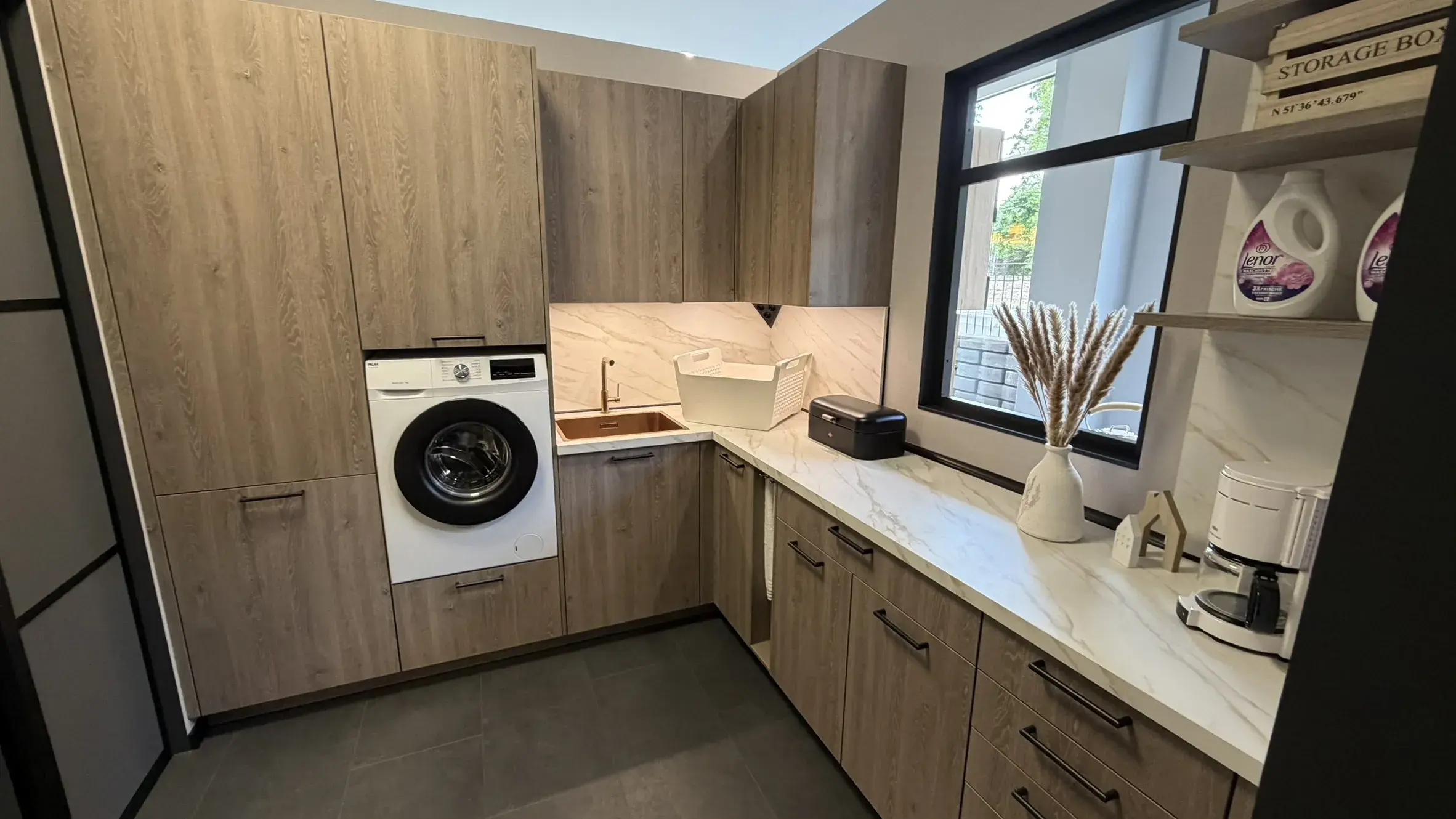Moderner Hauswirtschaftsraum mit Holzfronten, integrierter Waschmaschine, Spüle und großzügiger Arbeitsfläche