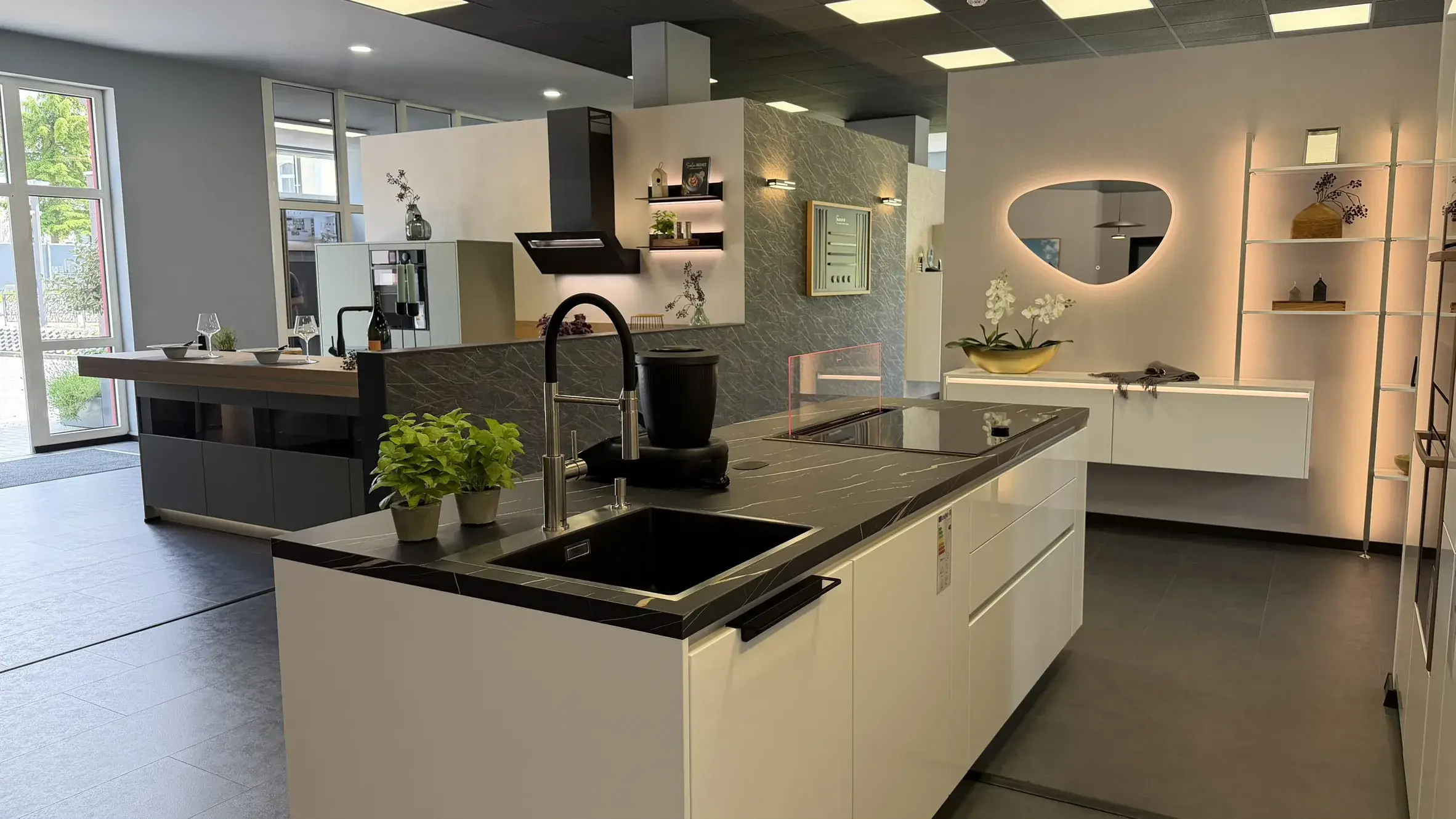 Moderne weiße Designküche mit Kochinsel, dunkler Arbeitsplatte, schwarzer Spüle und stilvoller Beleuchtung