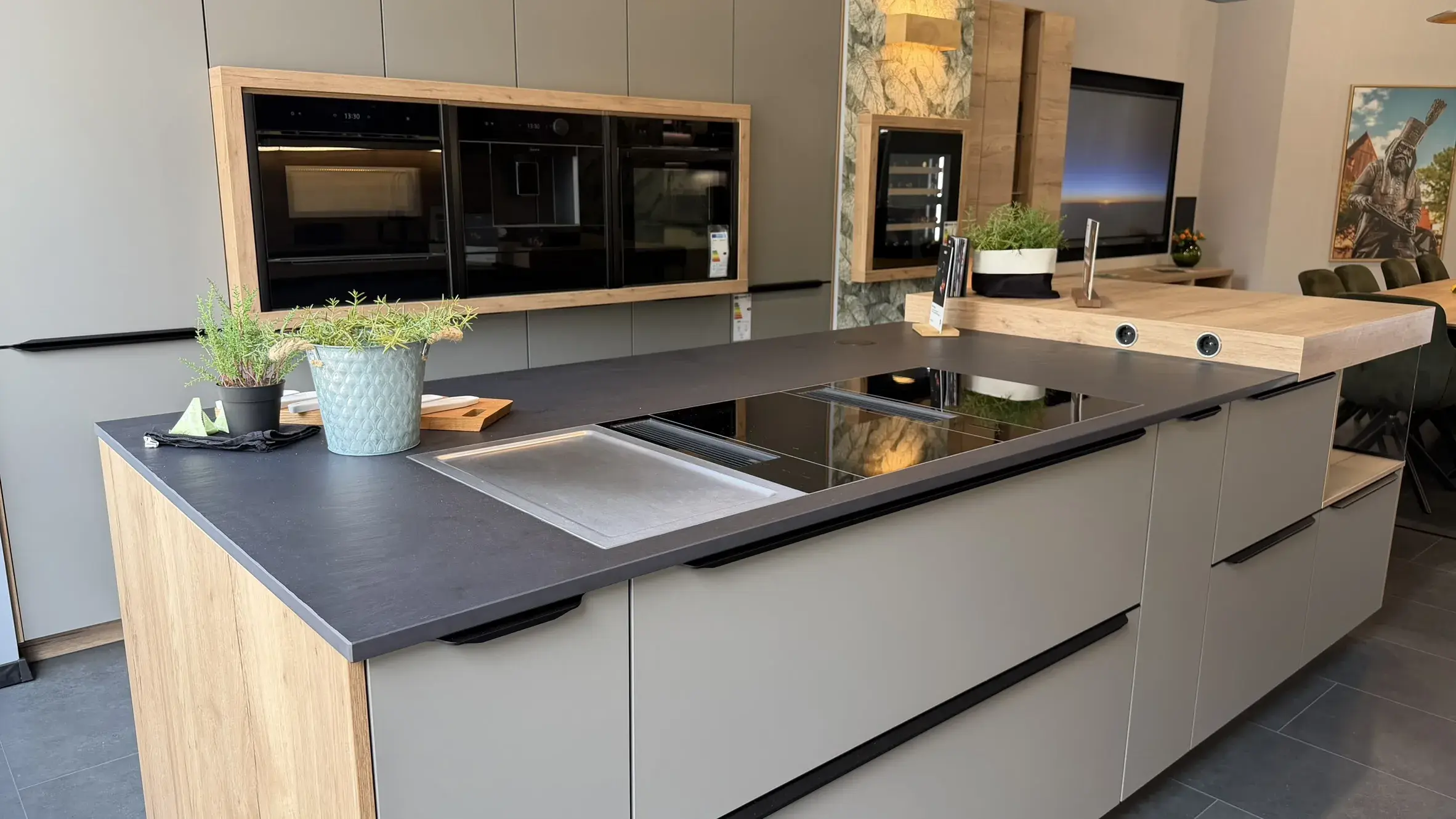 Moderne Designküche mit großer Kochinsel, grauen Fronten, warmen Holzelementen und integriertem Kochfeld mit Dunstabzug